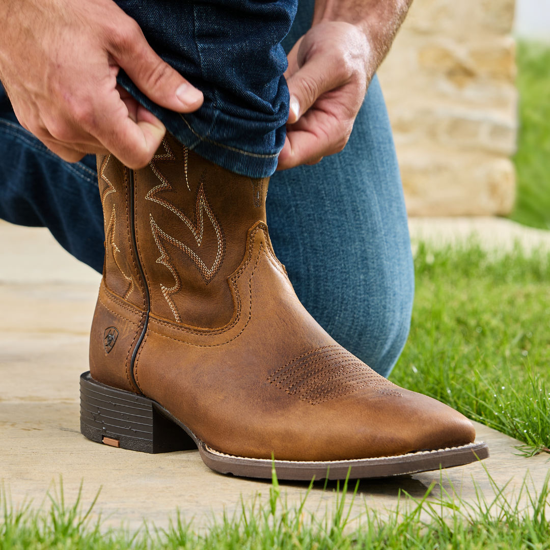 Man kneeling sliding blue denim jeans over to show Brown Leather Cowboy Boots 