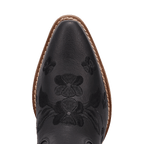 Close-up of the pointed toe of a black leather cowboy boot with floral tooling and a tan sole edge, shown on a white background.