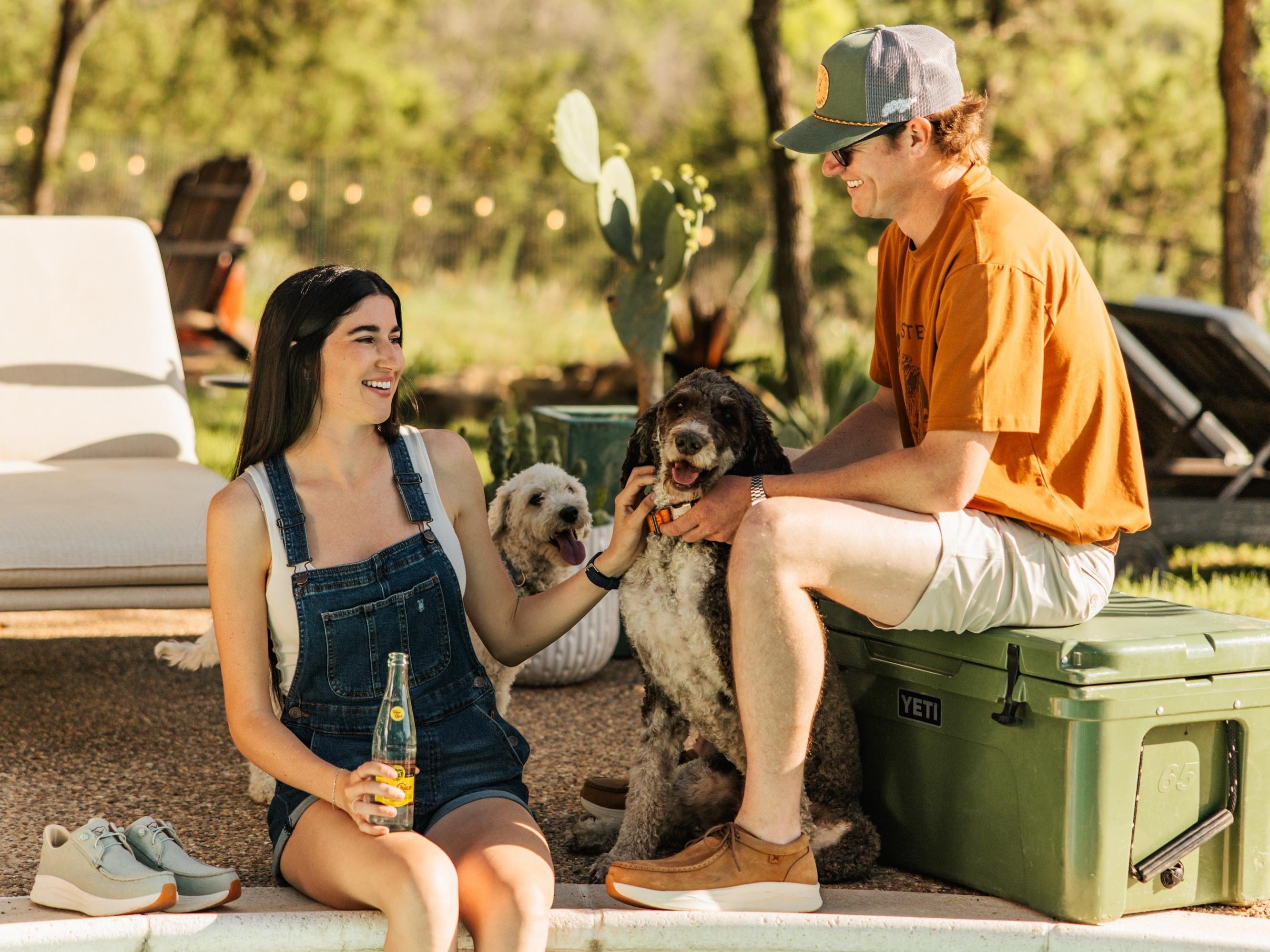 Two people sitting outdoors with two dogs, enjoying a casual moment.