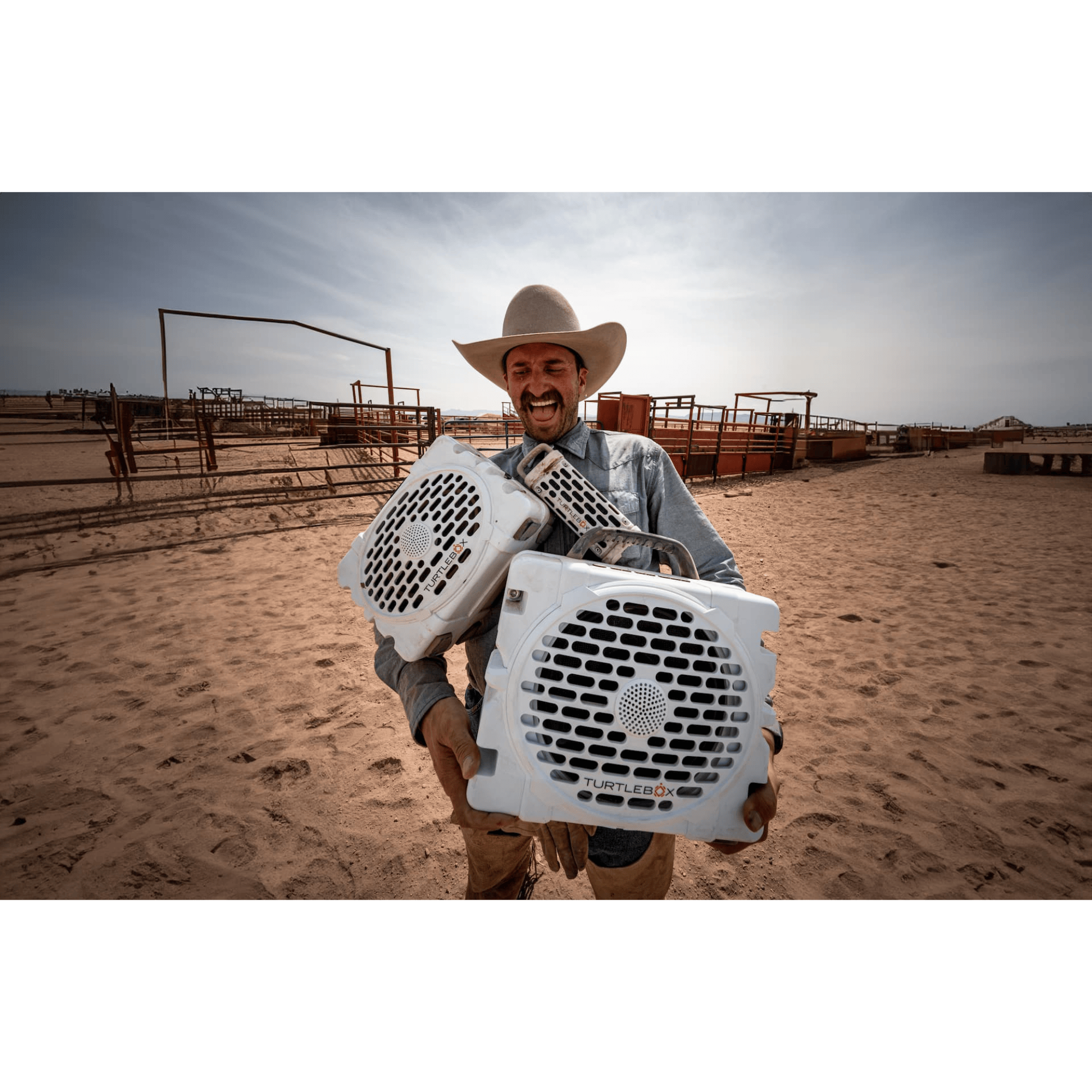 Man in cowboy hat holding two white animal crates in a desert setting