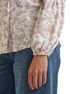 Close-up of a person wearing a cream blouse with a brown floral toile pattern and blue jeans, showing the sleeve and hand.