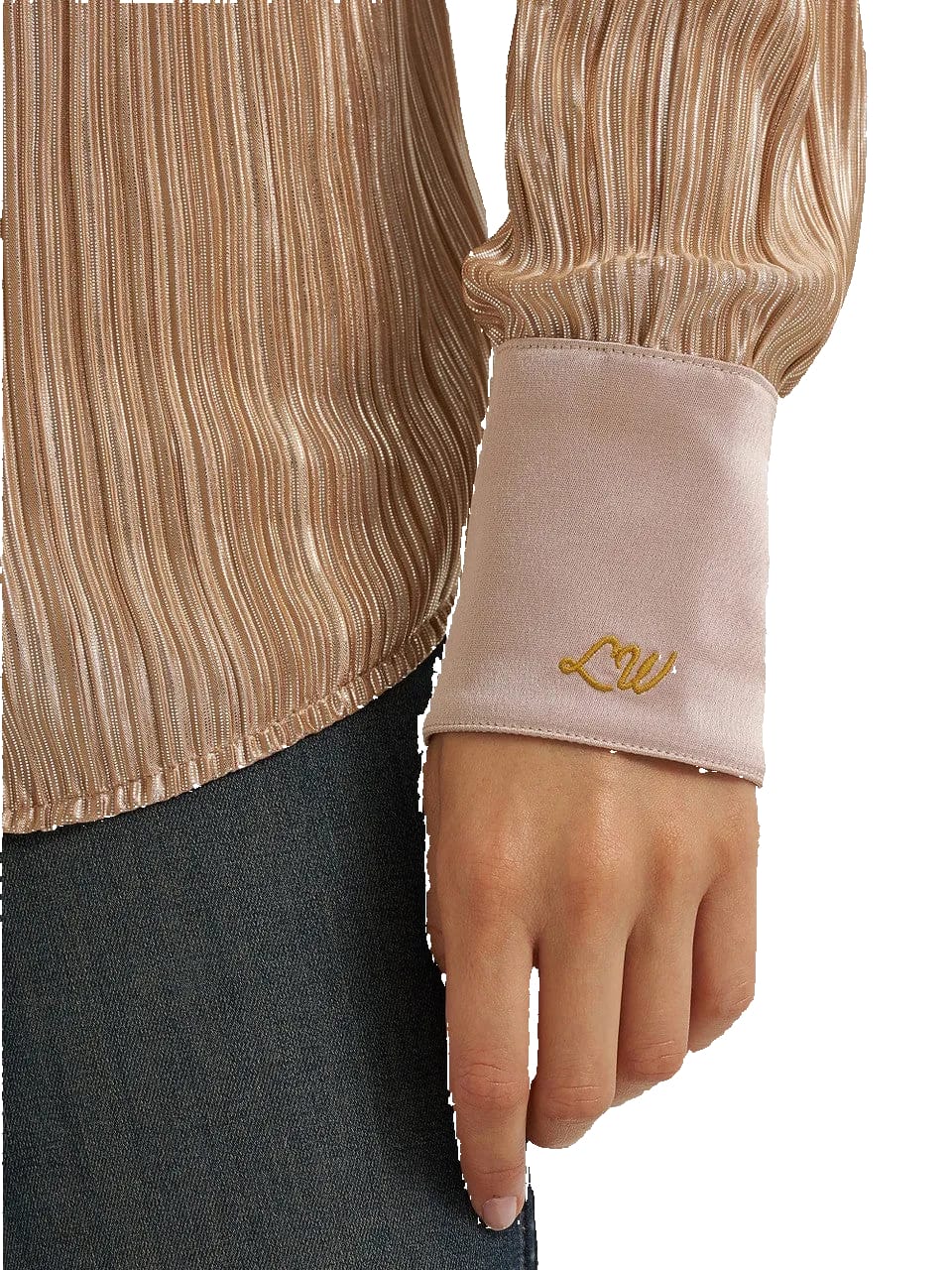 Close-up of a person wearing a champagne pleated long-sleeve blouse with a light blush pink satin cuff featuring gold embroidered initials 'LW', paired with dark gray trousers.