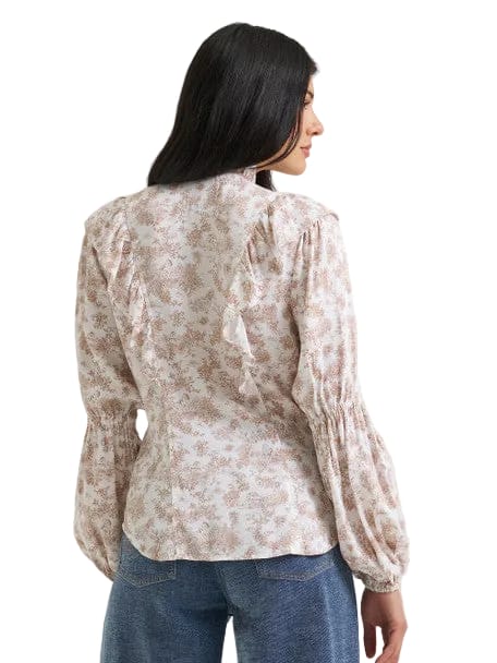 A woman shown from the back wearing a long-sleeve blouse with a beige and brown floral pattern, paired with blue jeans, against a light gray studio background.